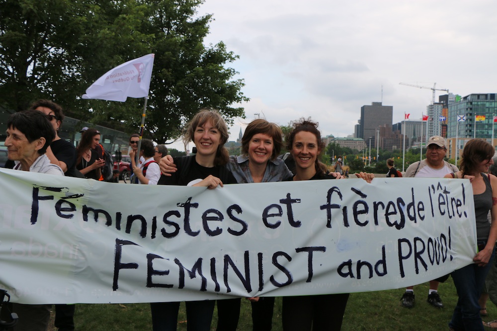 three women holding a banner "Feminist and proud"