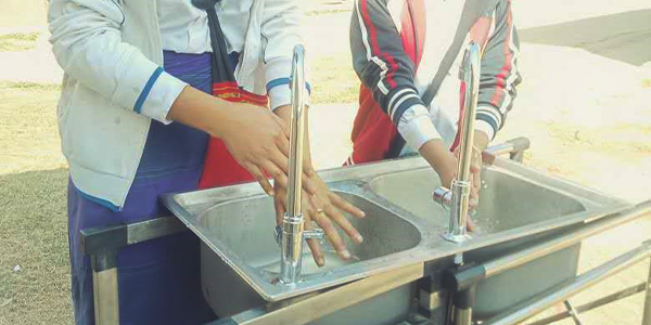 Two Burmese youth wash their hands at a basin. The water is flowing from the taps.