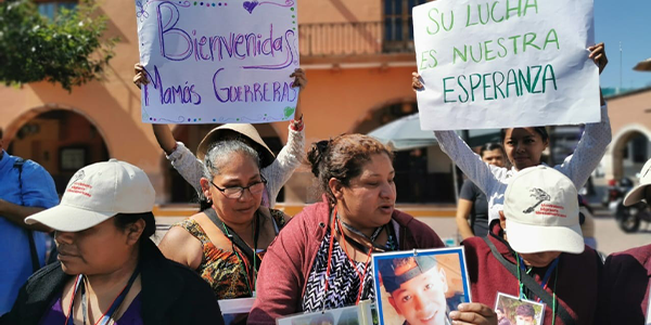 Women gather together outside holding signs that read 'Welcome mothers' and signs with photos of missing children