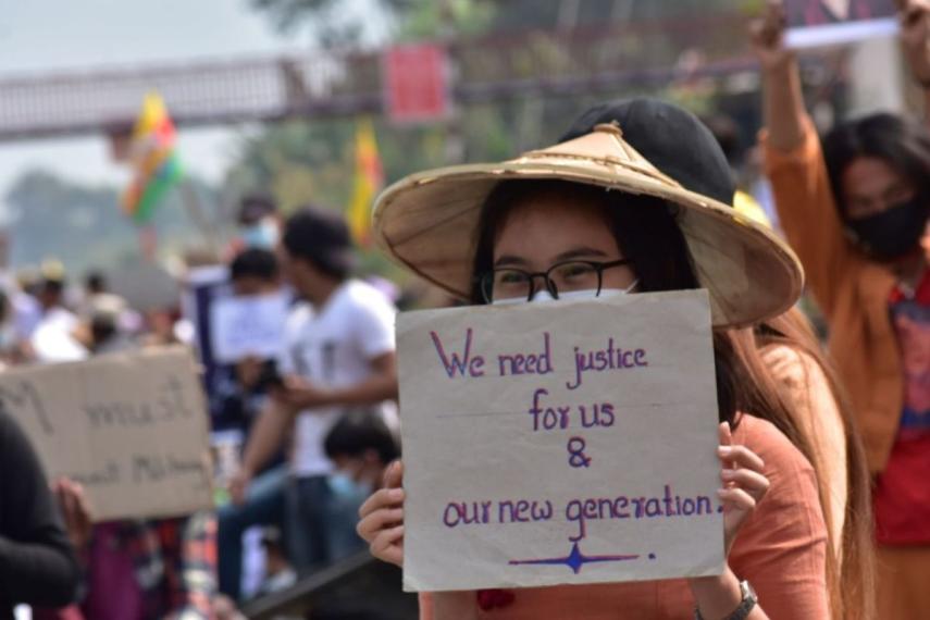 Photo of a person in a conical hat holding a sign with both hands. The sign says 