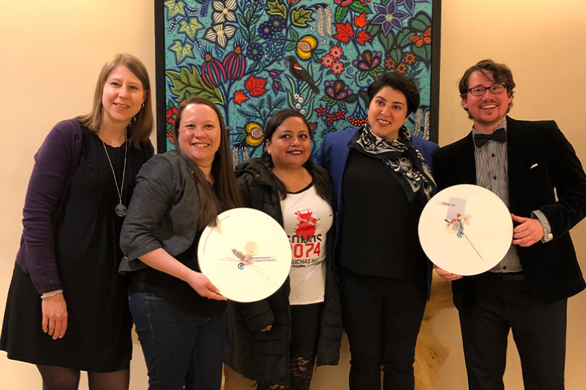 28.	Representatives from the National Aboriginal Council of Midwives and Clinic 554 stand with their 2019 Peter Gillespie Social Justice Award plaques and Peruvian activist Maria Ysabel Cedano. In the background is colourful Indigenous artwork.