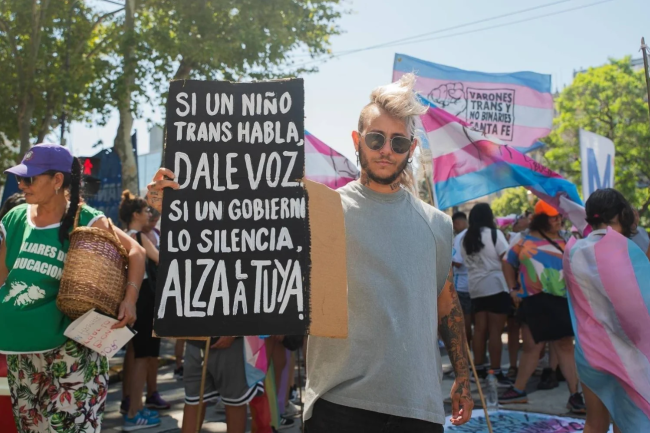 Un-e manifestant-e brandit une pancarte sur laquelle on peut lire en espagnol : « Si un enfant transgenre s'exprime, donnez-lui la parole. Si le gouvernement le réduit au silence, faites entendre votre voix. »